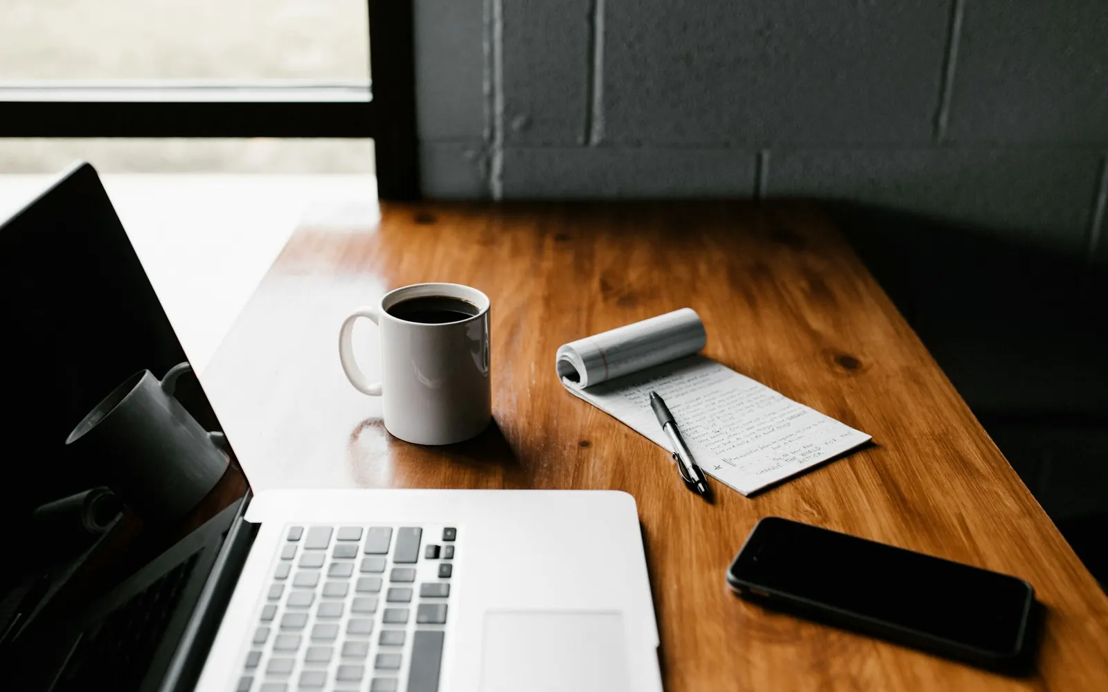 Illustrative photo: a laptop, a notepad and coffee on a wooden desk. Not a sample of the Paid Ads Copy Pack deliverable.