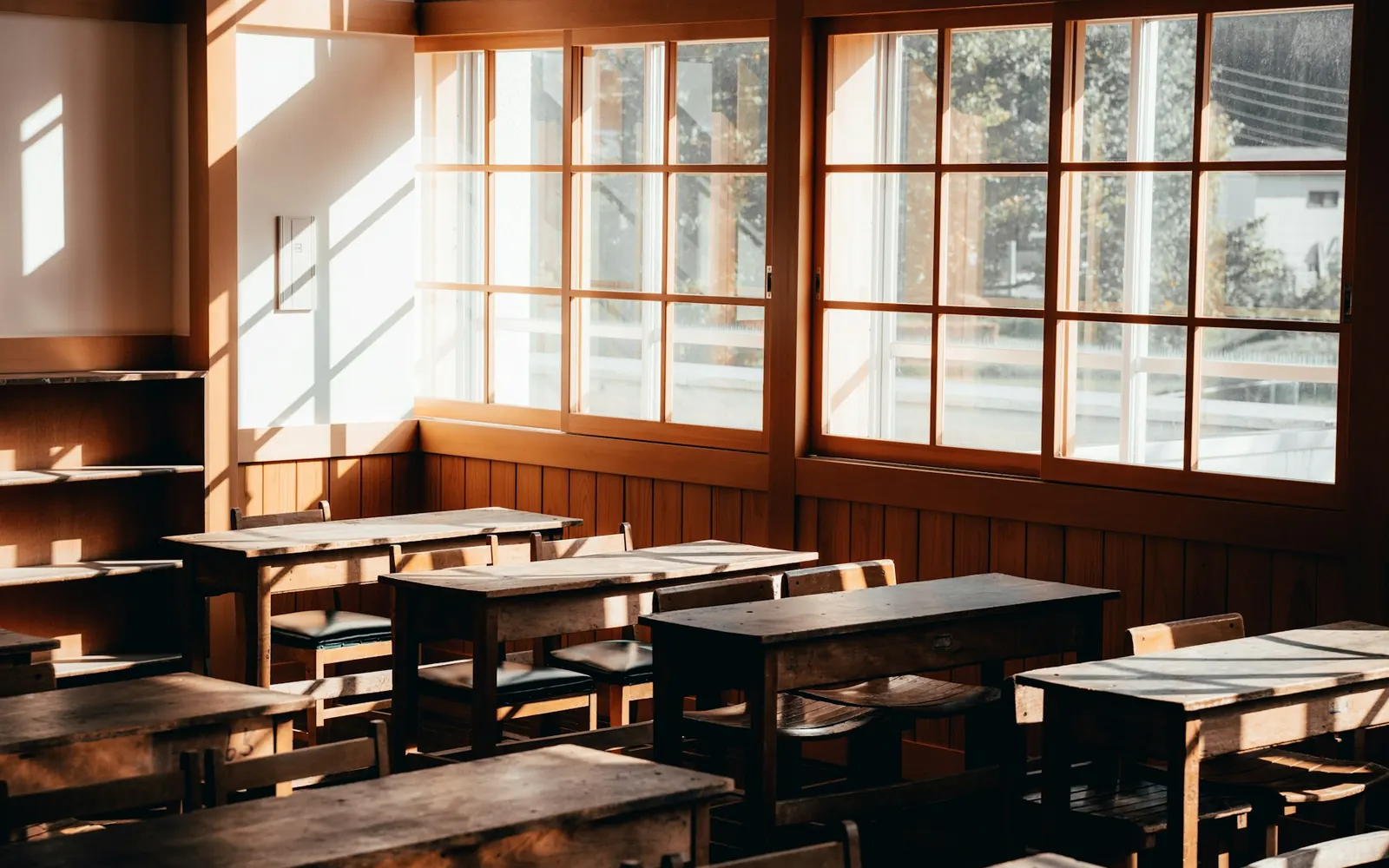 Illustrative photo: an empty sunlit classroom with wooden desks. Not a sample of the Training Course Outline & Materials deliverable.